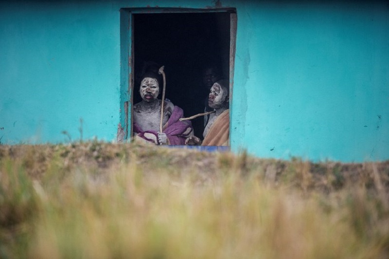 This file photo taken on July 13, 2017 shows traditional Xhosa initiates Fezikhaya Tselane (left), 20, and Khanyisile Mapope, 18, looking out from a door during a traditional initiation process, in a rural hut in the Coffee Bay area in Umtata, South Afric