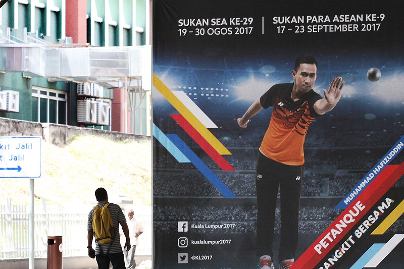 A man stands beside billboards featuring a picture of an athlete along the road nearby KL Sport City in Bukit Jalil ahead of KL 2017 Sea Games in Selangor Aug 7, 2017. u00e2u20acu201d Picture by Miera Zulyana