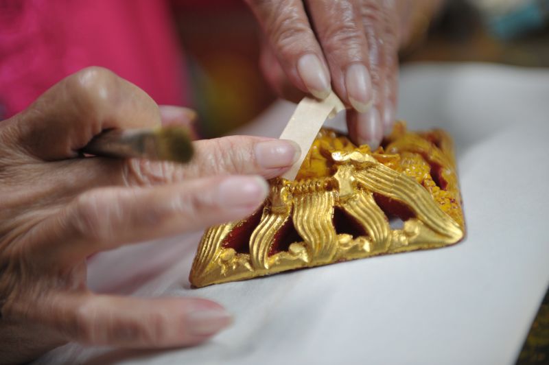 Yuen painstakingly layers each gold leaf onto the motifs of a furniture part.