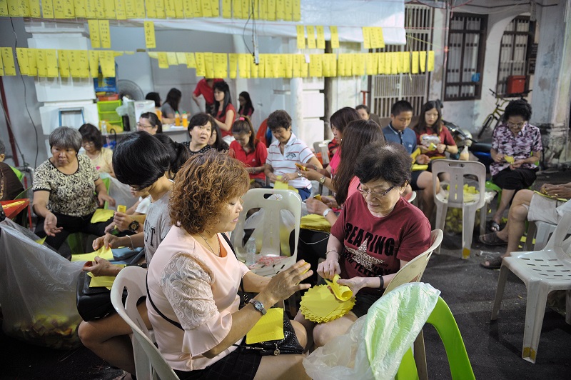 The community sitting down to fold joss paper into gold ingots as offerings to appease the spirits during Hungry Ghost Festival.