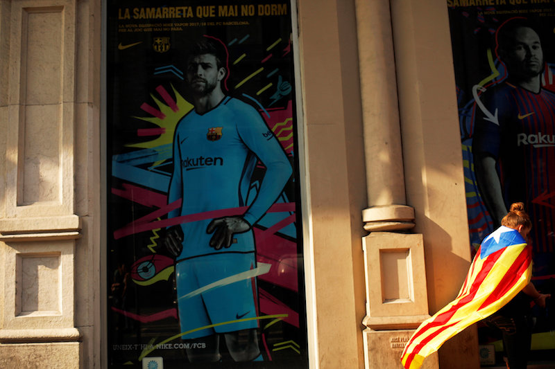A woman wrapped in an Estelada (Catalan separatist flag) stands next to an advertisement showing an image of FC Barcelona and Spainu00e2u20acu2122s national team player Gerard Pique in Barcelona October 3, 2017. u00e2u20acu201d Reuters pic