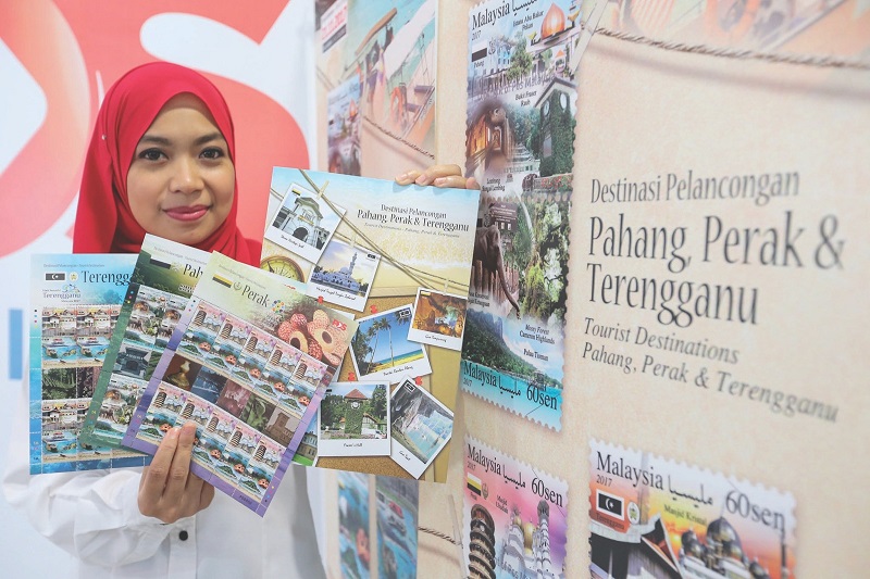 Pos Malaysia employee Asmahani Mohd Arshad showing the second edition of the u00e2u20acu02dcTourist Destinationsu00e2u20acu2122 stamp series and limited edition folders. u00e2u20acu201d Picture by Ahmad Zamzahuri