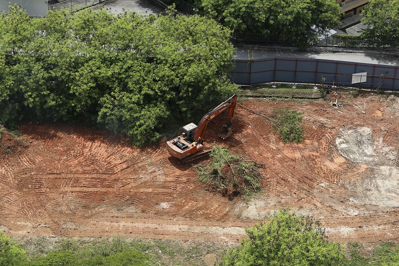 An excavator is seen clearing the land within the green hoardings of the project site. 