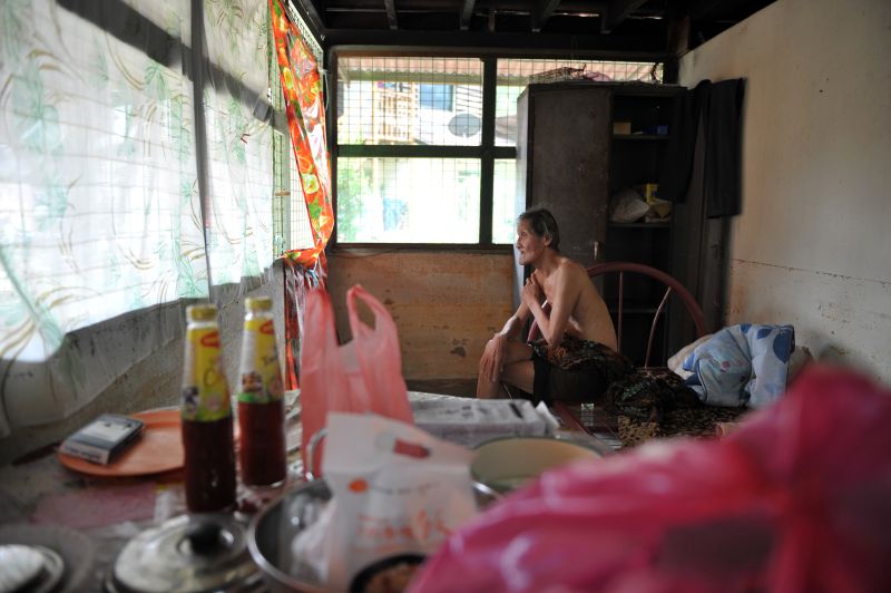Joseph Tan sits alone on his bare bed frame in his house in Kampung Sheikh Madar.
