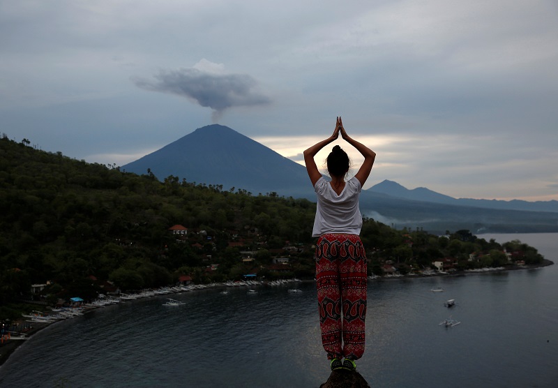 A tourist from Russia poses while a friend takes her photograph with Mount Agung volcano erupting in the background from Amed, Karangasem Regency, Bali December 1, 2017. u00e2u20acu201d Reuters pic