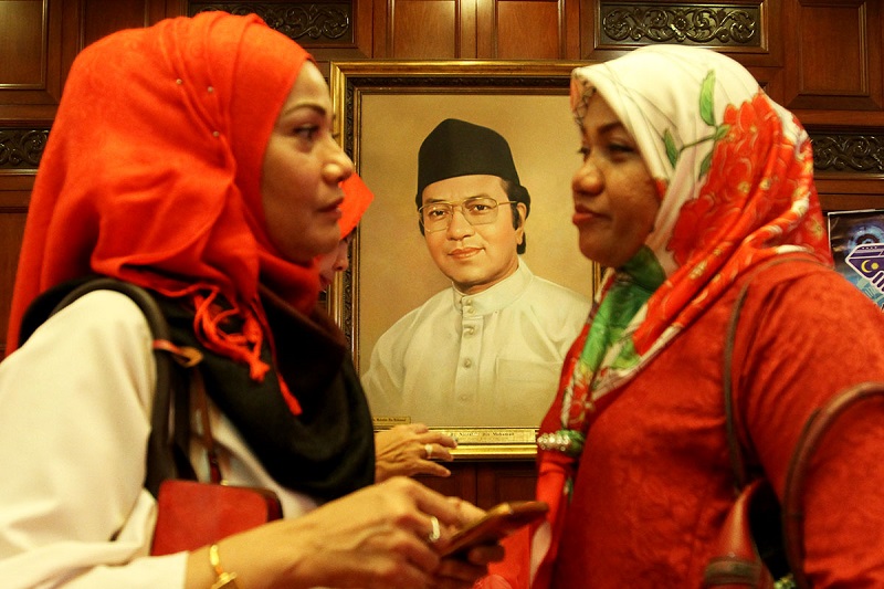 Women walk past a portrait of former prime minister Tun Dr Mahathir Mohamad during the 71st Umno General Assembly in Kuala Lumpur December 7, 2017. u00e2u20acu201d Picture by Miera Zulyana