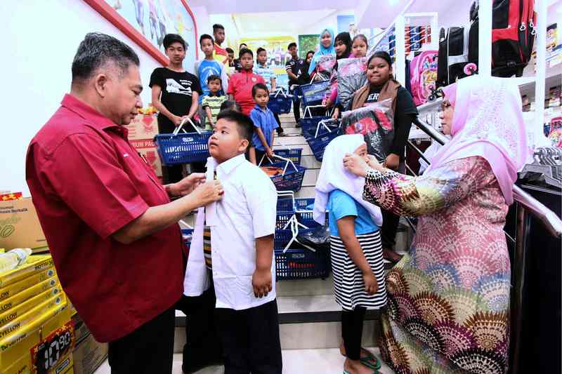 The late Lepar State Assemblyman Datuk Mohd Shohaimi Jusoh (left) and wife Datin Rohaizan Yatim (right) helping two students try school uniform at a supermarket, Kuantan December 29, 2017. u00e2u20acu201d Bernama pic