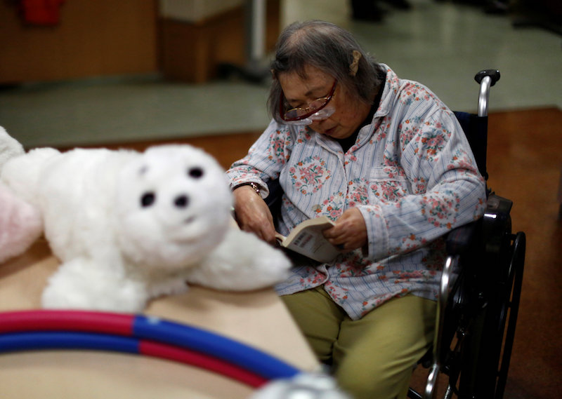 A resident reads a book during a session with ‘Aibo’, a pet dog robot, and ‘Paro’, a robot seal, at Shin-tomi nursing home in Tokyo February 2, 2018. — Reuters pic