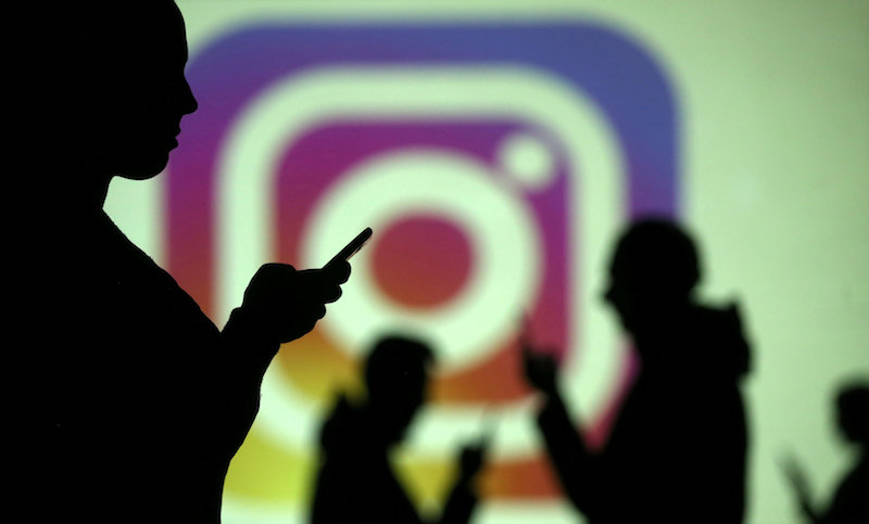 Silhouettes of mobile users are seen next to a screen projection of Instagram logo in this picture illustration taken March 28, 2018. u00e2u20acu201d Reuters pic