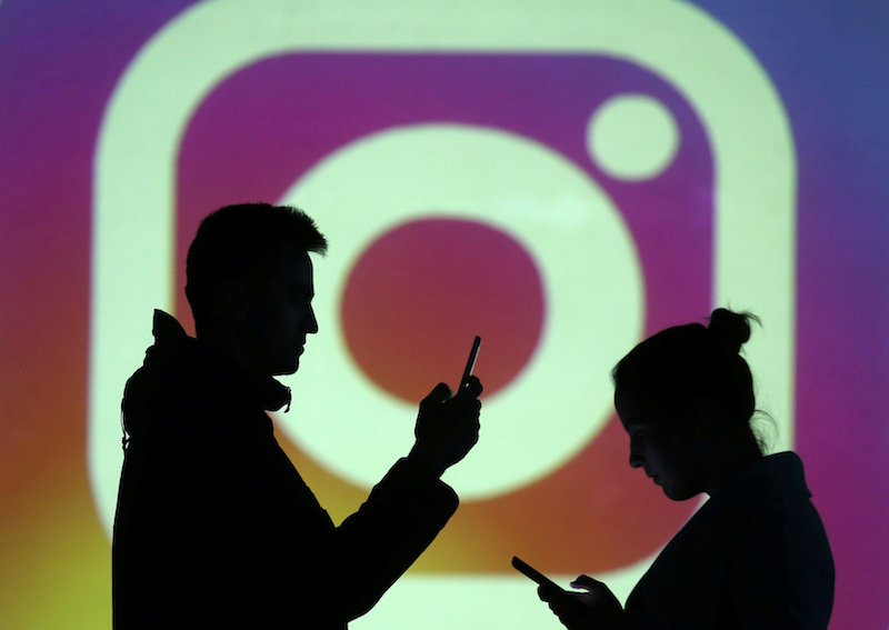 Silhouettes of mobile users are seen next to a screen projection of Instagram logo in this picture illustration taken March 28, 2018. u00e2u20acu201d Reuters pic
