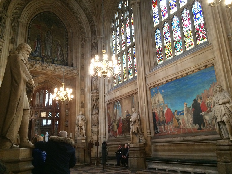 The inside of the UK Parliament building, called the Palace of Westminster, that features an oil painting of Queen Elizabeth commissioning Sir Walter Raleigh in 1584 to sail for America and to discover unknown lands.