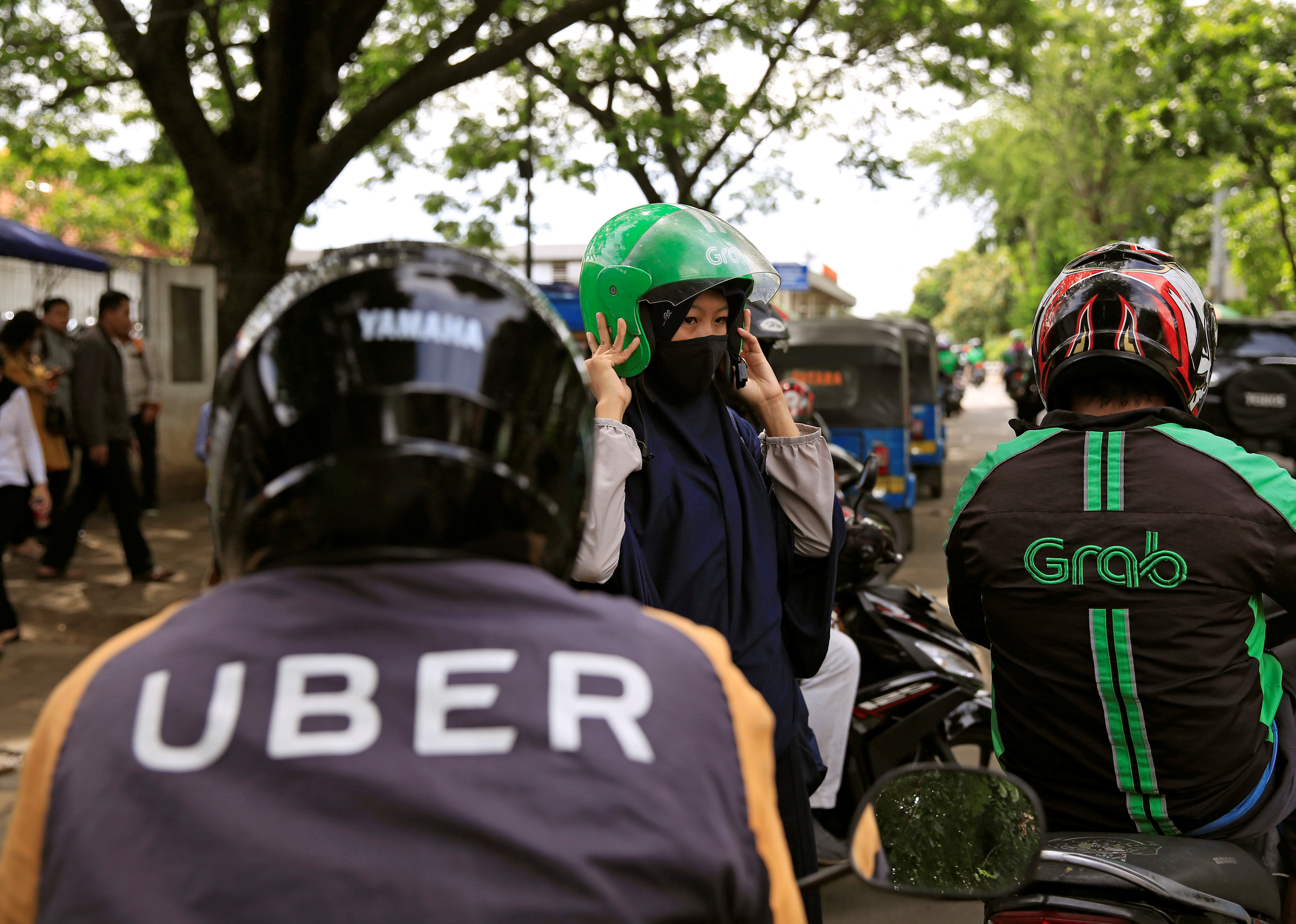 A passenger of Grab bike fixes her helmet next to Uber driver at Manggarai train station in Jakarta, Indonesia, March 26, 2018. u00e2u20acu201d Reuters pic