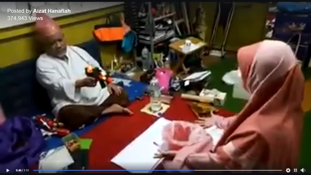 A screenshot of a video showing a bomoh using a toy gun replete with flashing lights and sound effects to u00e2u20acu02dctreatu00e2u20acu2122 a patient.