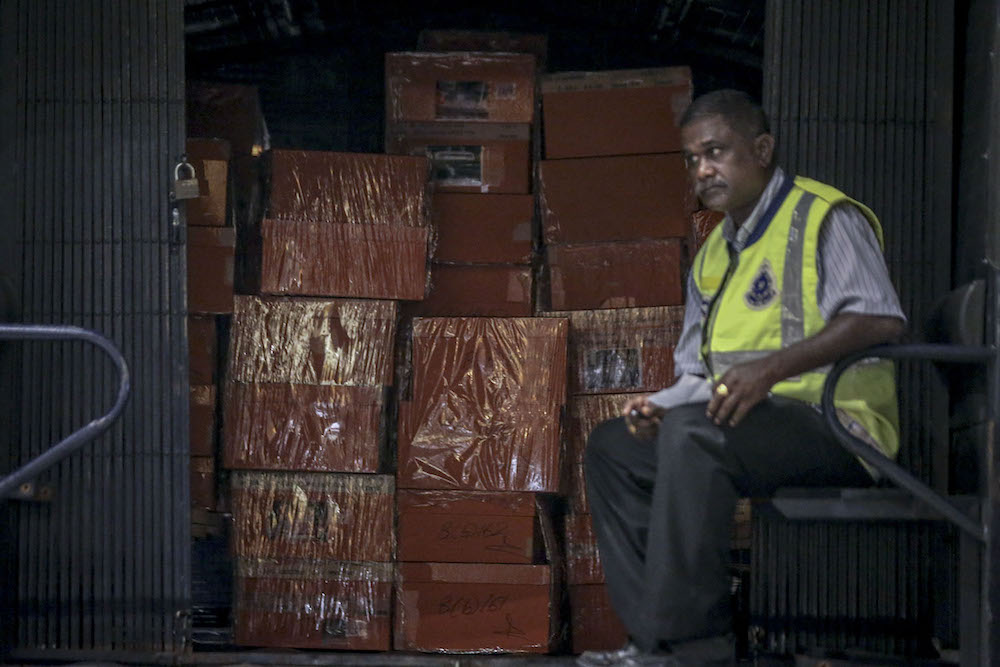 An investigator guards sealed boxes believed to contain luxury designer bags in a Black Maria outside Pavilion Residences in Kuala Lumpur May 18, 2018. — Picture by Hari Anggara  