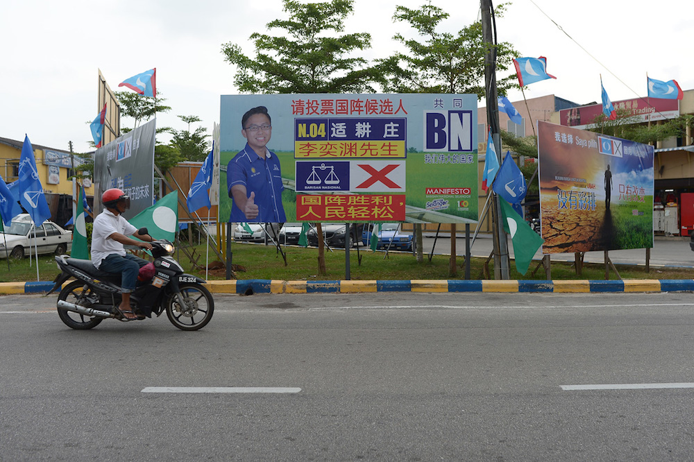 A villager rides a motorcycle past the BN flags and billboards in Sekinchan town. — Picture by Mukhriz Hazim