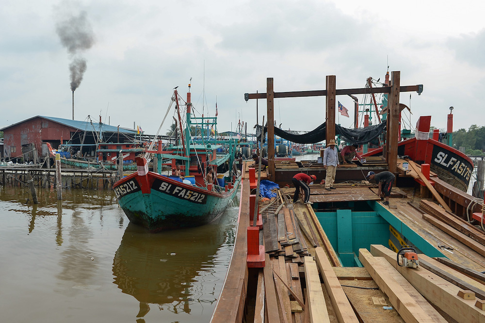 Men repair a fishing boat at a fishing jetty near Pantai Redang in Sekinchan. — Picture by Mukhriz Hazim