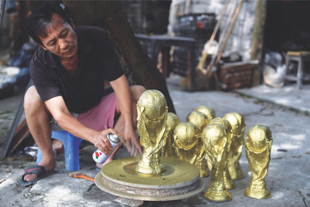 This picture taken on June 5, 2018 shows Vietnamese craftsman Vuong Hong Nhat spraying gold colour paint on a plaster model of the football World Cup trophy at a workshop in Hanoi. u00e2u20acu201d AFP pic