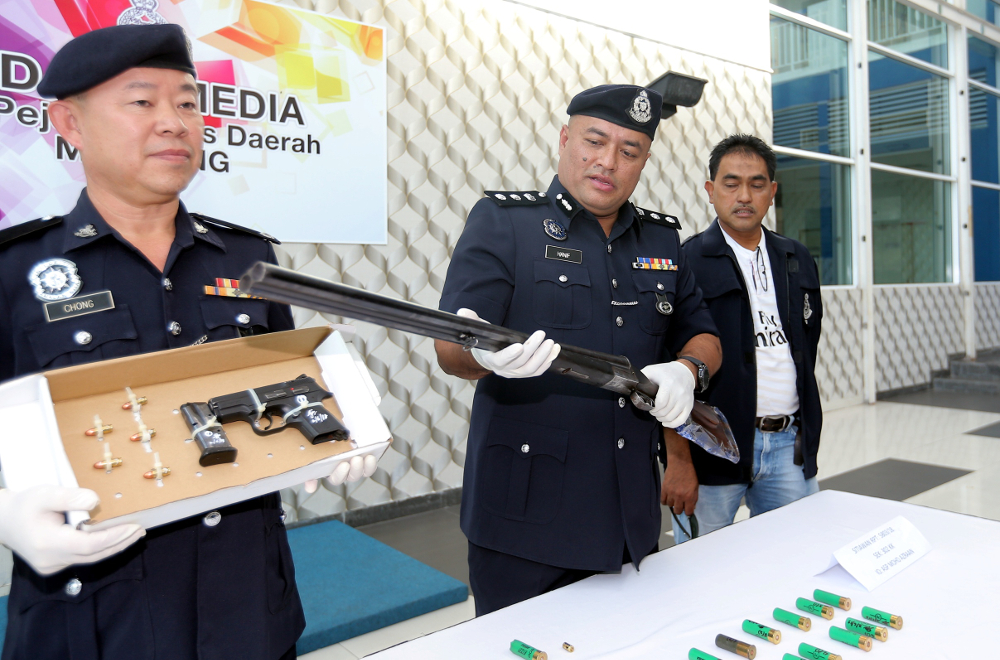 District Police Chief Muhammad Hanif Othman displays the shot gun used by the suspect to kill the victim, while his Deputy Chong Boo Khim displays the pistol used by the suspect to kill himself in Manjung June 2, 2018. — Picture by Farhan Najib