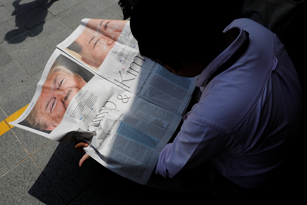 A journalist reads a local newspaper showing an article on the summit between US President Donald Trump and North Korean leader Kim Jong Un near St. Regis hotel in Singapore June 11, 2018. u00e2u20acu201d Reuters pic