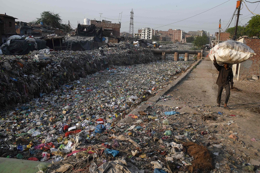 This photo taken on May 30, 2018 shows a man carrying a bag containing plastic recyclable items next to a sewage drain canal full of garbage in the Taimur Nagar slum area in New Delhi. u00e2u20acu201d AFP pic