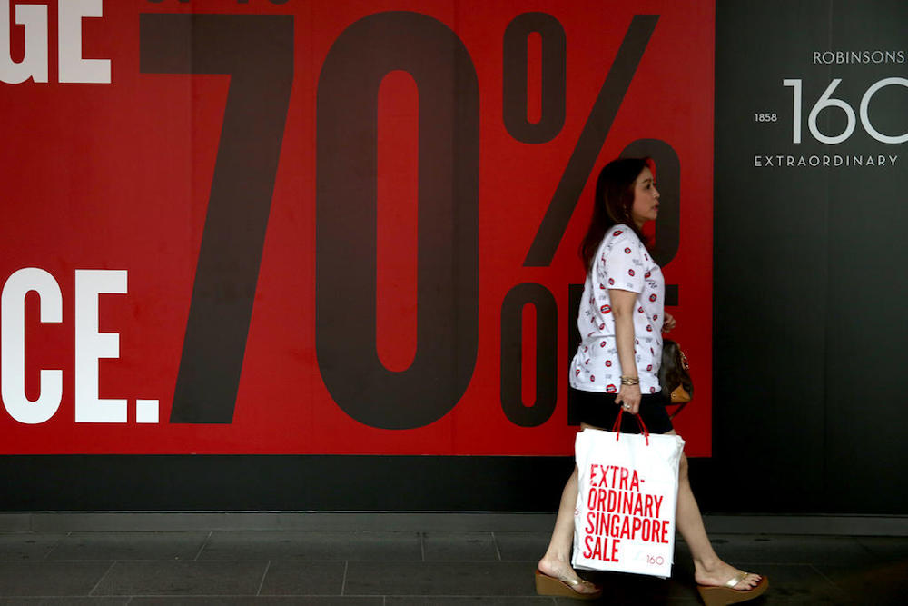 A woman walks by a poster promoting slashed prices outside Robinsons along Orchard Road during the Great Singapore Sale. u00e2u20acu201d TODAY pic