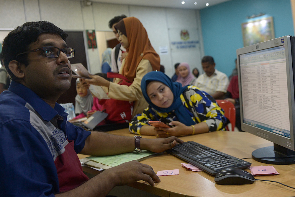 Mugheelan Sellathoray (left) keys in data for people who came to get their citizenship rights during ‘Program Mendaftar Anak Malaysia’ in Bandar Bukit Tinggi July 8, 2018. — Picture by Mukhriz Hazim