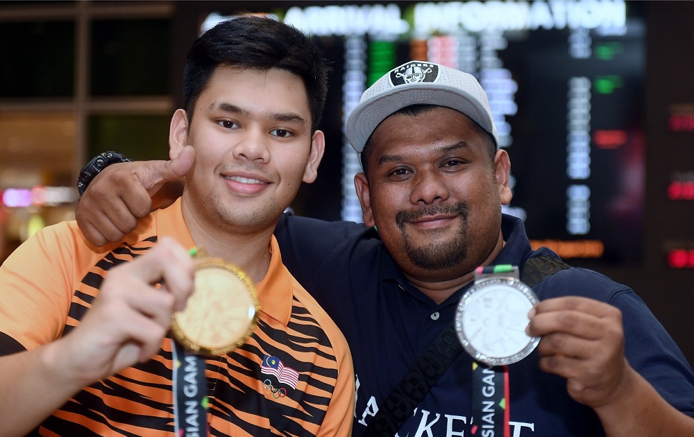 National tenpin bowler Muhammad Rafiq Ismail (left) and his brother pose for pictures with his gold medal upon arrival at KLIA August 28, 2018. u00e2u20acu201d Bernama pic