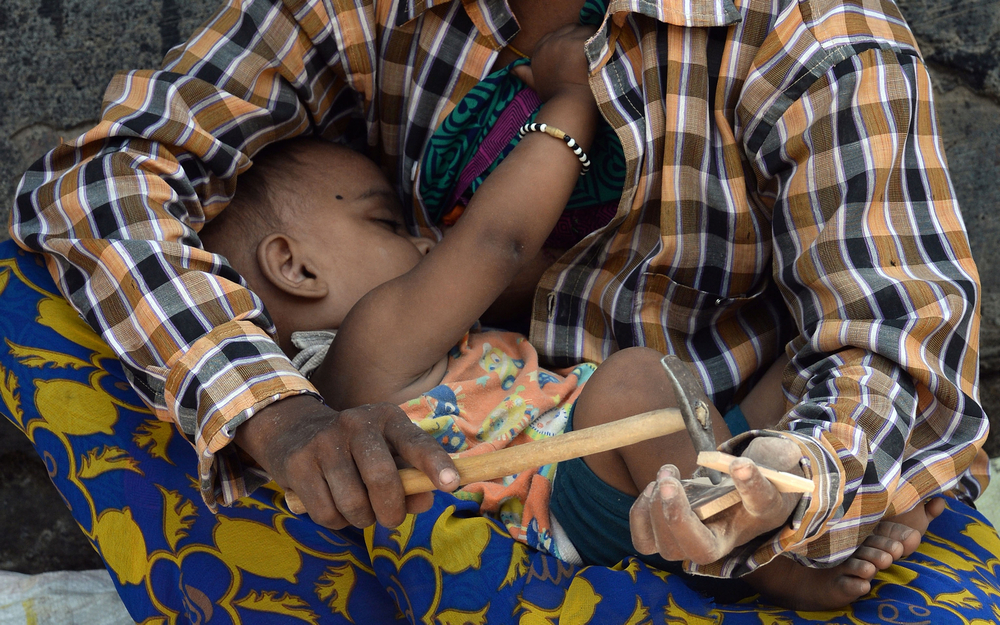 An Indian labourer breastfeeds her child as she breaks apart broken tiles outside an under-construction apartment building in Mumbai, India. u00e2u20acu201d AFP pic