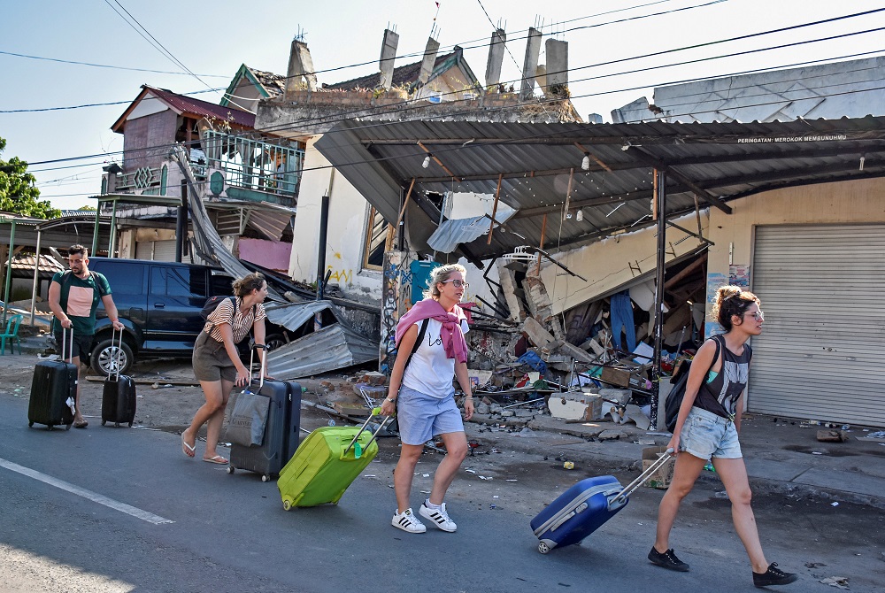 Foreign tourists pull their suitcases as they walk past damaged buildings following a strong earthquake in Pemenang, North Lombok, Indonesia August 6, 2018 in this photo taken by Antara Foto. u00e2u20acu201d Antara Foto/Ahmad Subaidi/ via Reuters 