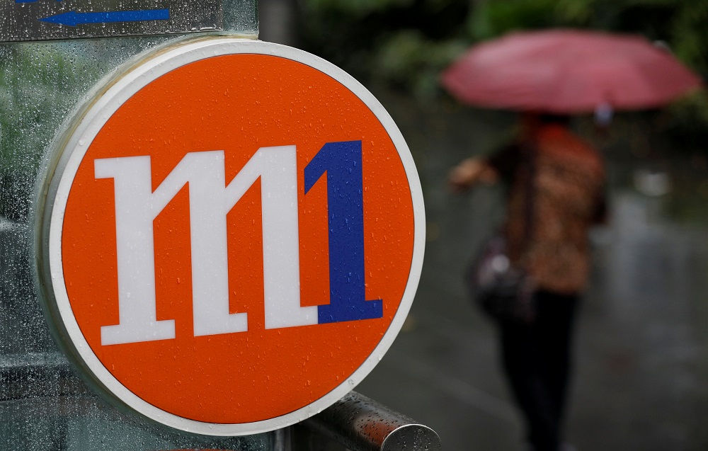 A woman with an umbrella passes an M1 sign in Singapore April 7, 2017. u00e2u20acu201d Reuters pic