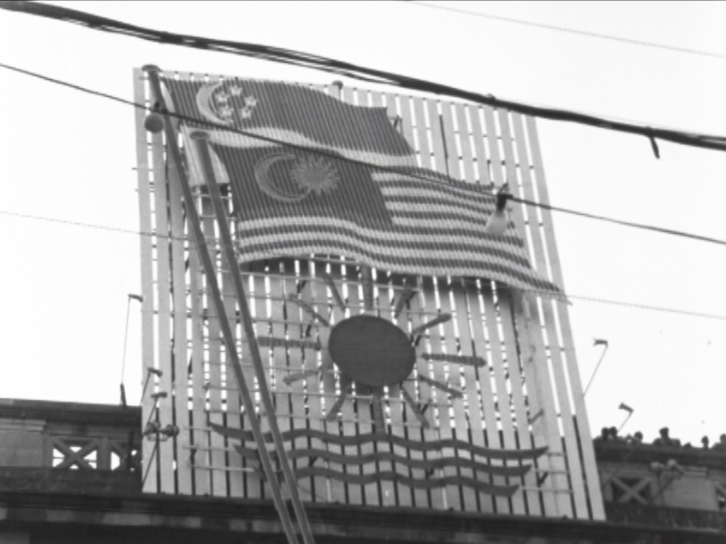Singapore’s flag is shown here with Malaysia’s flag. Singapore was part of Malaysia from September 16, 1963 until August 9, 1965. — Screen capture via Reuters archive footage
