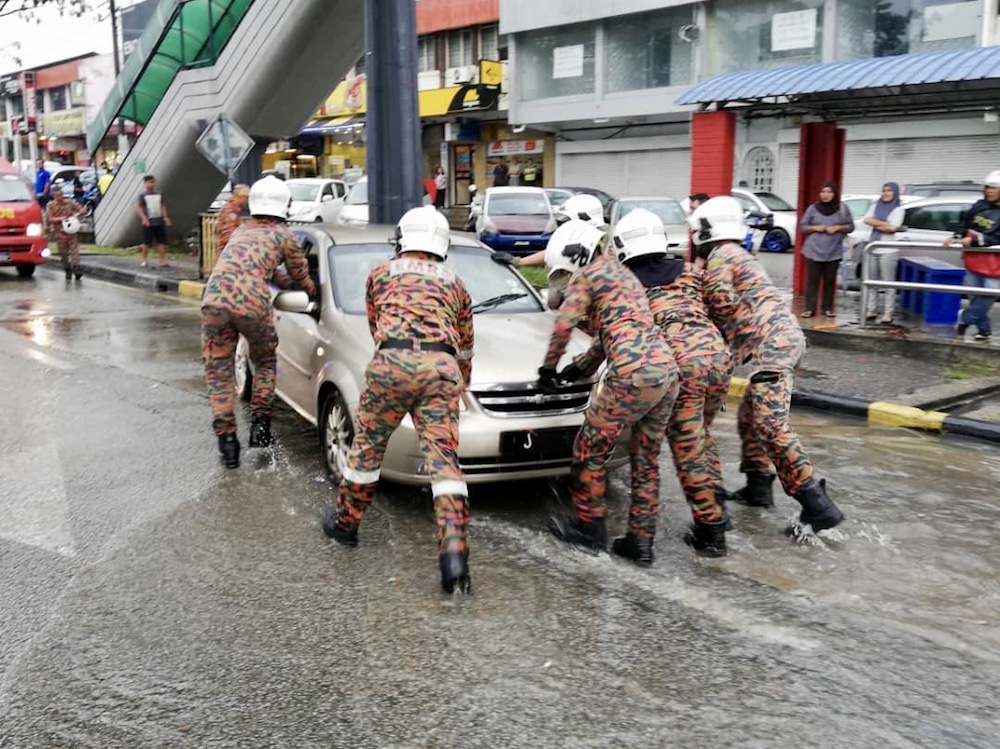 Firemen push the car in which two elderly women became trapped due to flash flooding along Jalan Tebrau in Taman Sentosa today. u00e2u20acu201d Picture courtesy of Johor Fire and Rescue Department