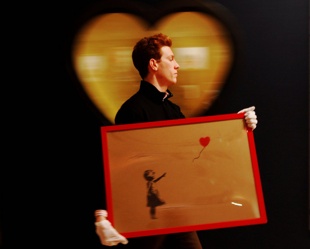An employee walks with Banksy's ,Girl and Balloon, 2009, at Bonhams auction house in London March 23, 2012. 