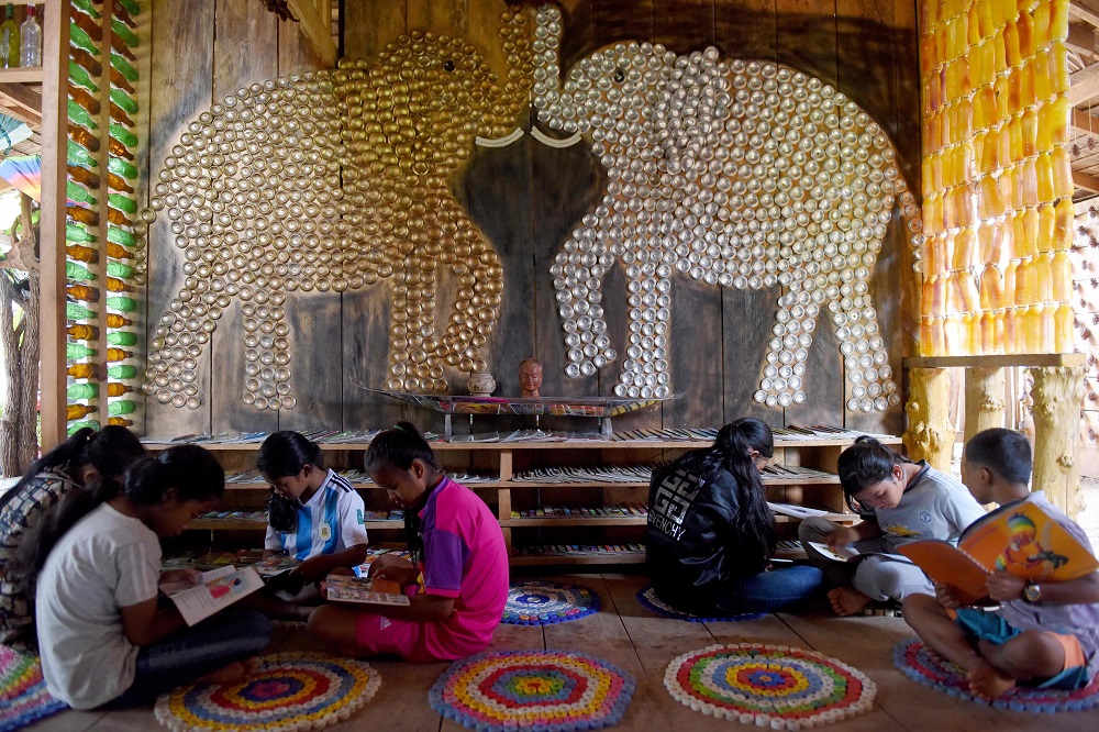 This photo taken on October 1, 2018, shows students reading books at the library of Coconut School decorated by two elephant figures made from aluminium cans at Kirirom national park in Kampong Speu province. — AFP pic  