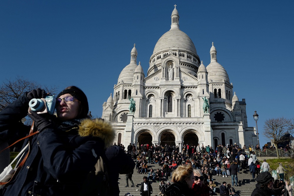 This file photo shows a woman taking photographs as people sit in front of the Sacre Coeur Basilica in Montmartre in Paris February 25, 2018. u00e2u20acu201d AFP pic