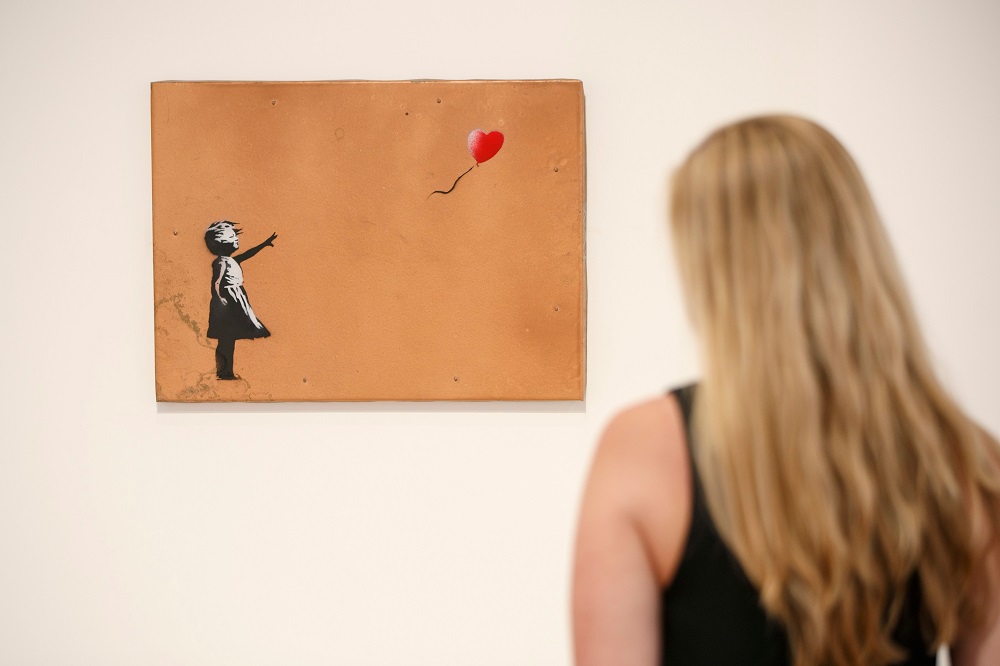 A gallery assistant poses with u00e2u20acu02dcGirl with Balloonu00e2u20acu2122 2006 artwork by Banksy at Lazinc Gallery in London July 11, 2018. u00e2u20acu201d AFP pic