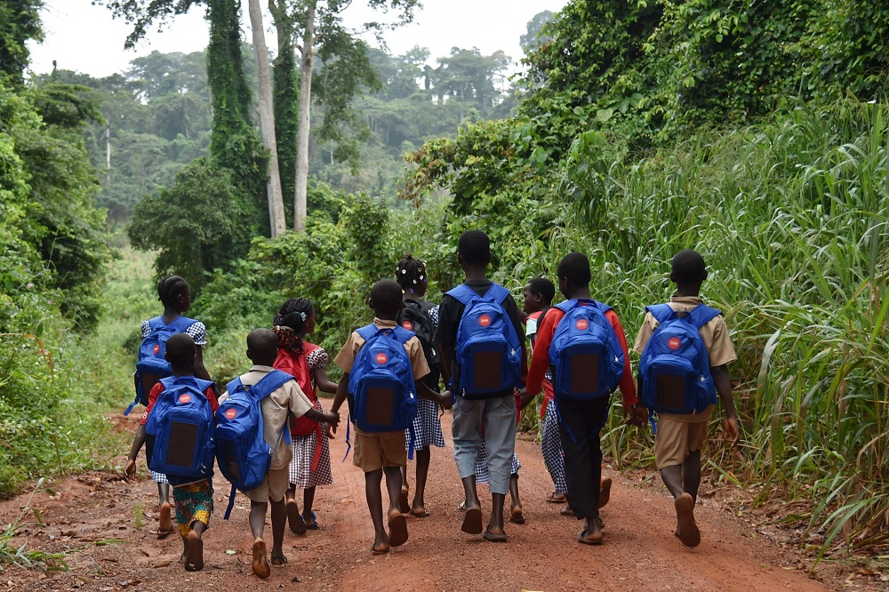 Ivorian schoolchildren walk to school carrying backpacks fitted with a connected lamp powered by solar panels near their village in the southeastern Rubino district September 17, 2018. — AFP pic