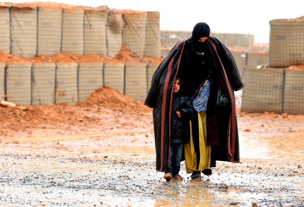 In this file photo taken on March 1, 2017, a Syrian refugee from the informal Rukban camp walks in the rain as she shelters a young child outside a UN-operated medical clinic immediately on the Jordanian-side. u00e2u20acu201d AFP pic  