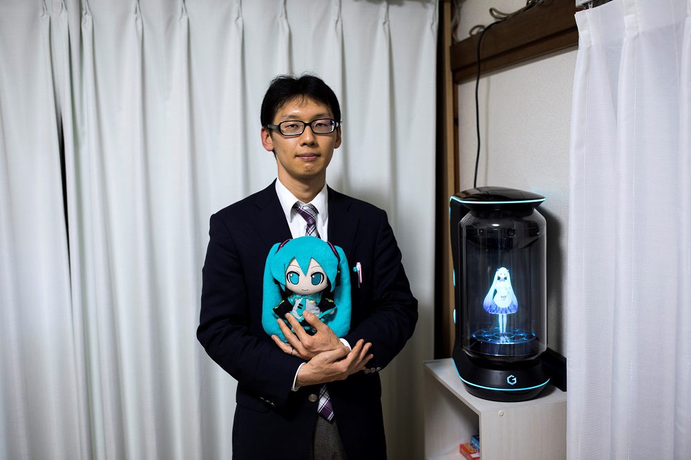 In this photograph taken on November 10, 2018, Japanese Akihiko Kondo poses next to a hologram of Japanese virtual reality singer Hatsune Miku as he holds the doll version of her at his apartment in Tokyo, a week after marrying her. u00e2u20acu201d AFP pic