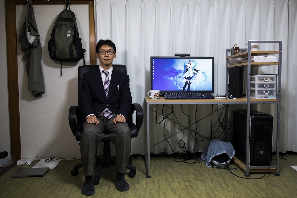 In this photograph taken on November 10, 2018, Japanese Akihiko Kondo poses next to an image of Japanese virtual reality singer Hatsune Miku, on a screen at his apartment in Tokyo, a week after marrying her. — AFP pic