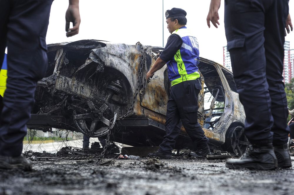 Police personnel help to clear the burnt wreckage of a car outside the Sri Maha Mariamman Devasthanam temple, November 27, 2018. u00e2u20acu2022 Picture by Shafwan Zaidon