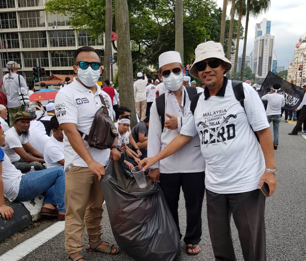 Tumpat parliamentary candidate representative Tengku Yusuf Tengku Ismail throws rubbish into a bag held by volunteer rubbish collectors Azmi Ismail and Abdul Rashid, with the latter two showing that democracy does not have to be literally messy. — Picture by Azril Annuar