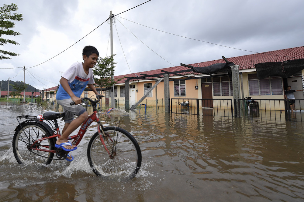 A boy cycles along a flooded street in Kemaman December 13, 2018. u00e2u20acu201d Bernama pic