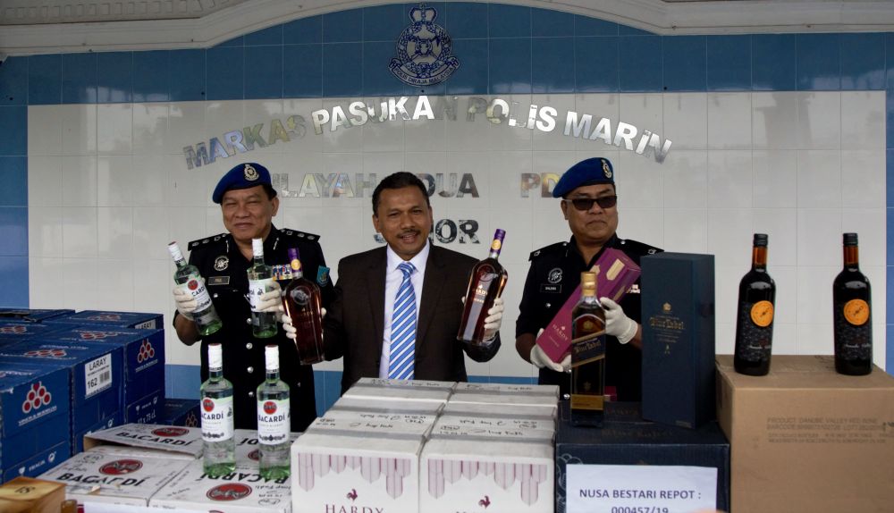 Senior Assistant Commissioner Mohd Yusoff Mamat (centre) is pictured with the seized liquor at the Region Two marine police base in Tampoi January 16, 2019. u00e2u20acu201d Picture by Roysten Rueben