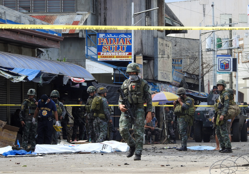 Policemen and soldiers keep watch as body bags (in white), containing the remains of blast victims, as seen in a cordoned area outside a church in Jolo, Sulu province on the southern island of Mindanao, on January 27, 2019. u00e2u20acu201d AFP pic
