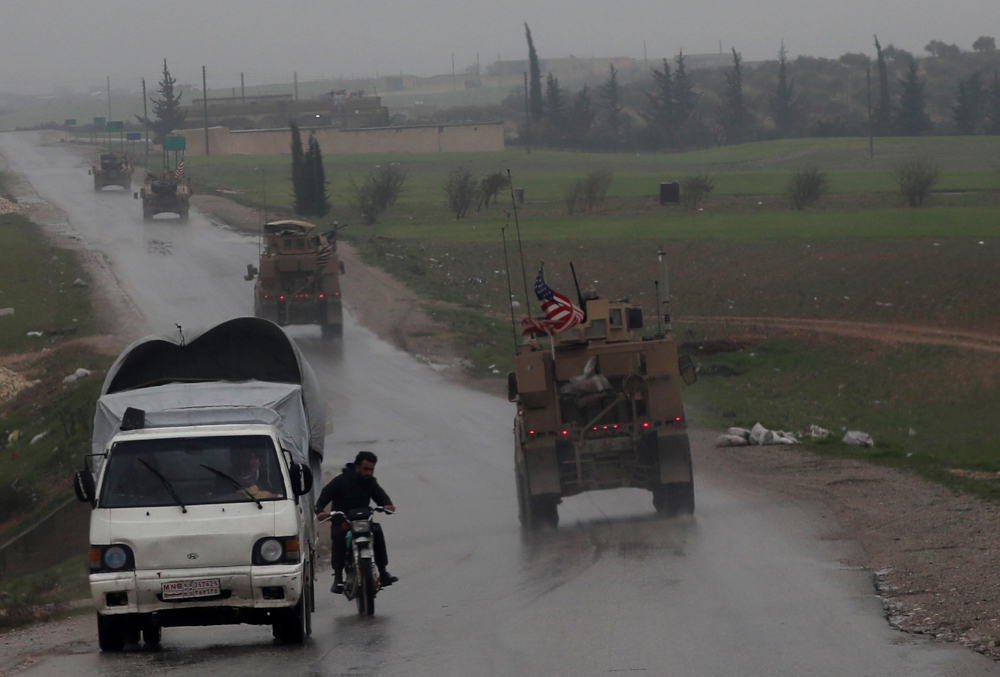 Inhabitants of Syriau00e2u20acu2122s northern city of Manbij drive past a line of US military vehicles on December 30, 2018. Russian military police have begun patrolling around the city, moving into an area once held by US-backed Kurdish forces. u00e2u20acu201d AFP pic