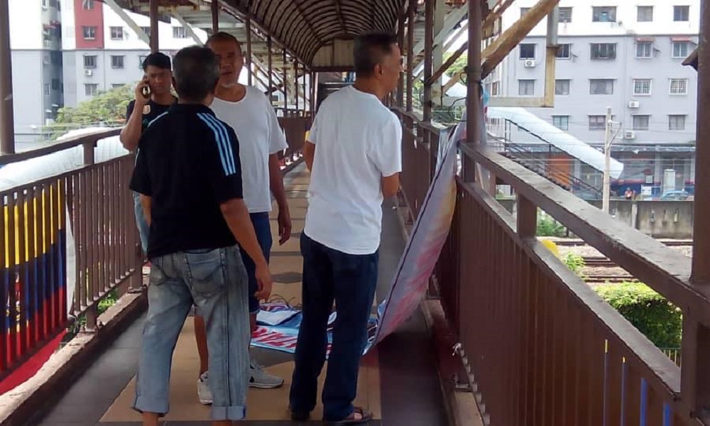 PKR members are seen taking down the political banners placed at the pedestrian bridge on Jalan Bangsar. -- Picture via Facebook/Fahmi Fadzil