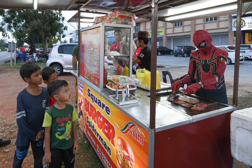 Fakhrul Fahmie Ishak, who makes burgers in his Spiderman costume, has become an attraction as he helps his brother Ahmad Ridhuan at his burger stall in Kampung Raja, Besut. u00e2u20acu201d Bernama pic  