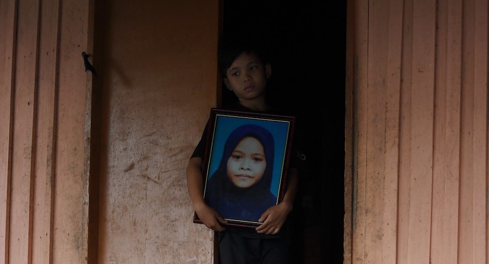 Nine-year-old Mohamad Khairy holds a photo of his 11-year-old sister Siti Masitah Ibrahim, whose body was dumped in an oil palm plantation, in Kampung Tanjung Medang Hilir, Pekan February 11, 2019. u00e2u20acu201d Bernama pic