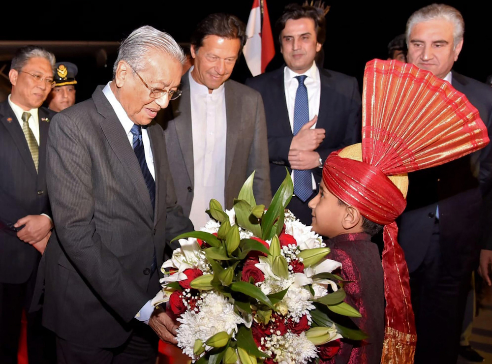 Malaysian Prime Minister Tun Dr Mahathir Mohamad receives a bouquet of flowers from a boy as Pakistani Prime Minister Imran Khan looks on at Nur Khan Base in Rawalpindi March 21, 2019. u00e2u20acu201d AFP pic